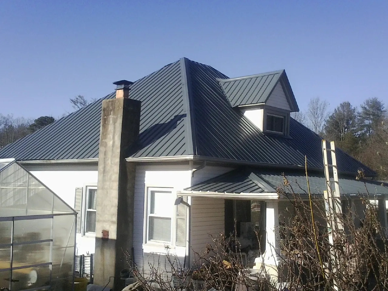 Dark blue standing seam metal roof on a white farmhouse with dormer — Slate & Tile Roof Repair by Roofing Brothers in Lake Powell