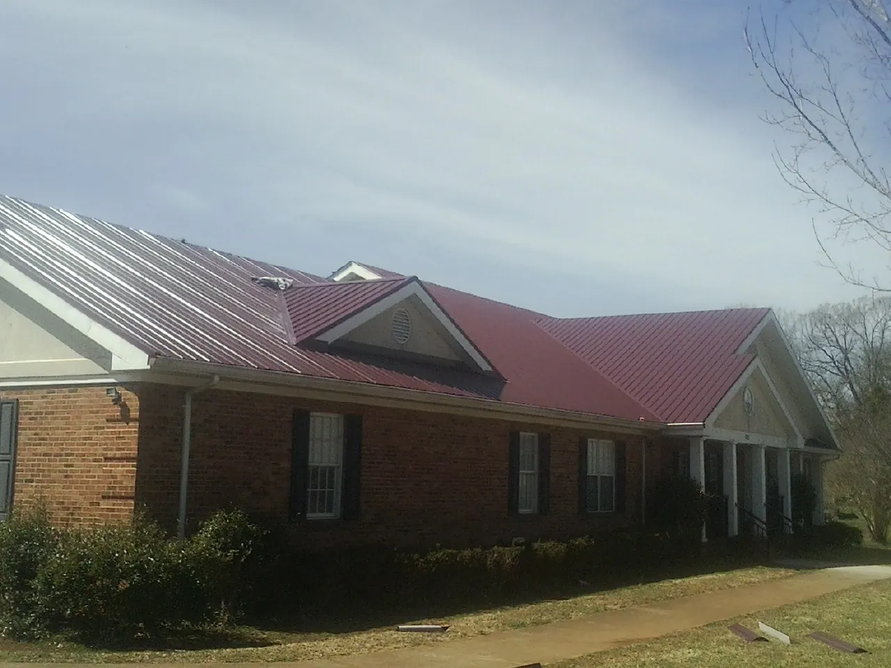 Red metal roof with gabled entries on a long brick building, from a Hail Damage Roof Repair job in Lake Powell