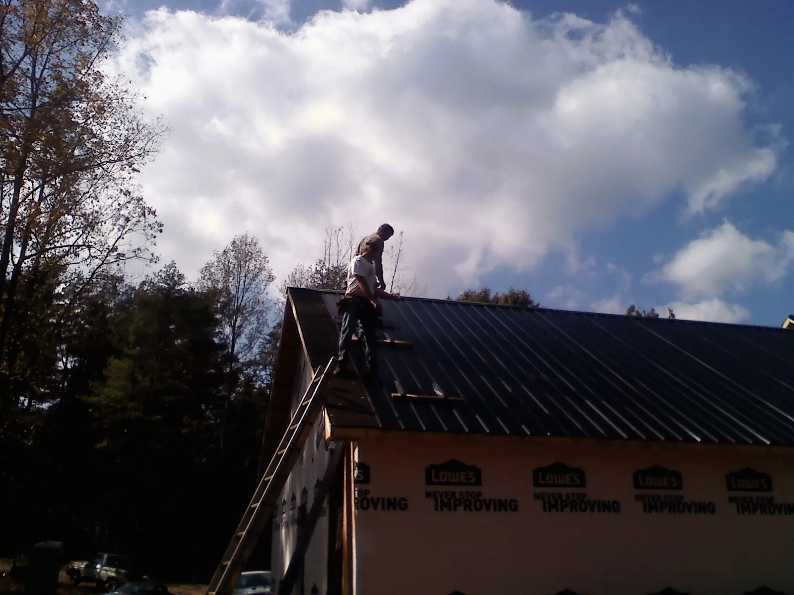 Roofer fastening dark metal panels high against a cloudy sky, from a Roof Inspection job in Lake Powell